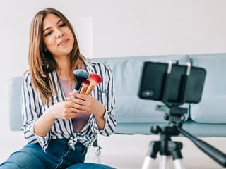 Influenser filmer sminkevideo med mobil og stativ som del av influensermarkedsføring på sosiale medier
