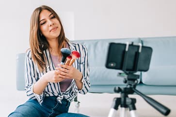 Influenser filmer sminkevideo med mobil og stativ som del av influensermarkedsføring på sosiale medier