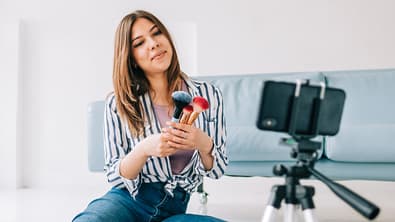 Influenser filmer sminkevideo med mobil og stativ som del av influensermarkedsføring på sosiale medier