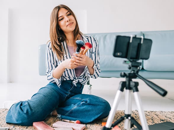 Influenser filmer sminkevideo med mobil og stativ som del av influensermarkedsføring på sosiale medier