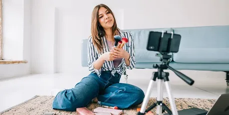Influenser filmer sminkevideo med mobil og stativ som del av influensermarkedsføring på sosiale medier