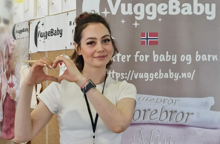 Store owner Emilia Wendelbo forming a heart with her hands in front of the VuggeBaby stand, with name-embroidered towels beside her