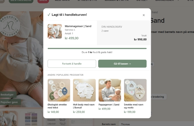 The added to cart confirmation window at VuggeBaby, with the product, free shipping progress, buttons on to the checkout and four recommended bestsellers